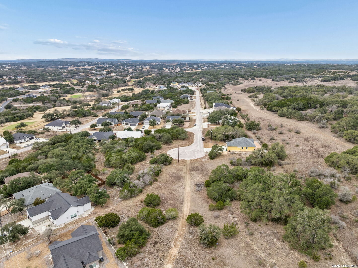 Aerial view of homes and open scrubland along a neighborhood road in Blanco, Texas.