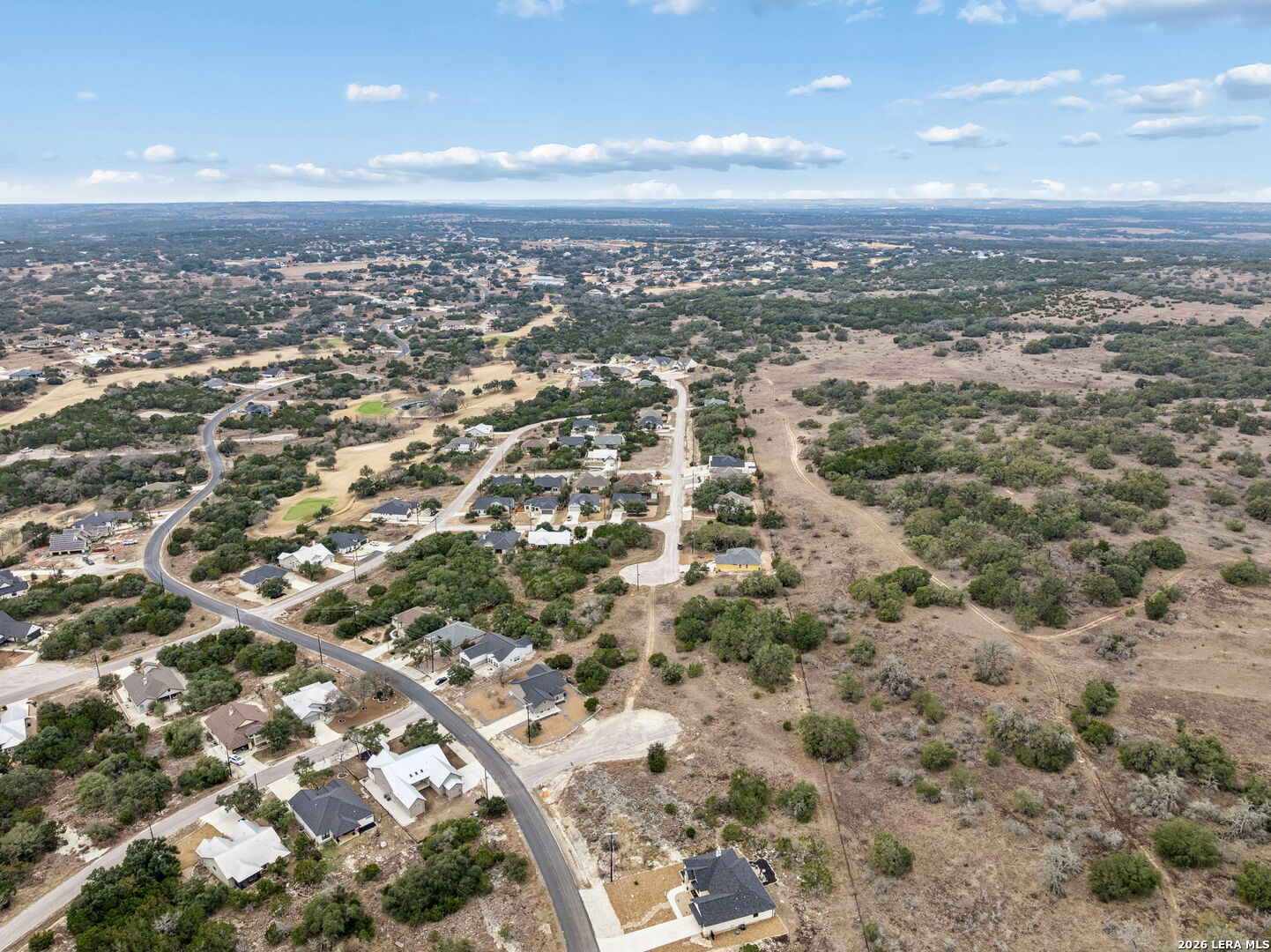 Aerial view of homes and winding roads beside open scrubland.