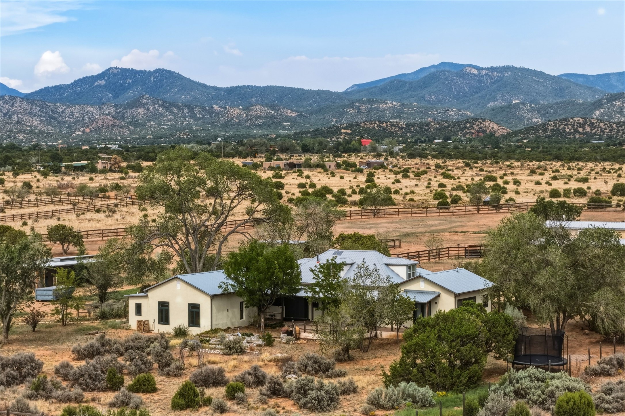 Aerial view of a ranch-style home amid dryland landscaping, fenced fields, and mountain ranges.