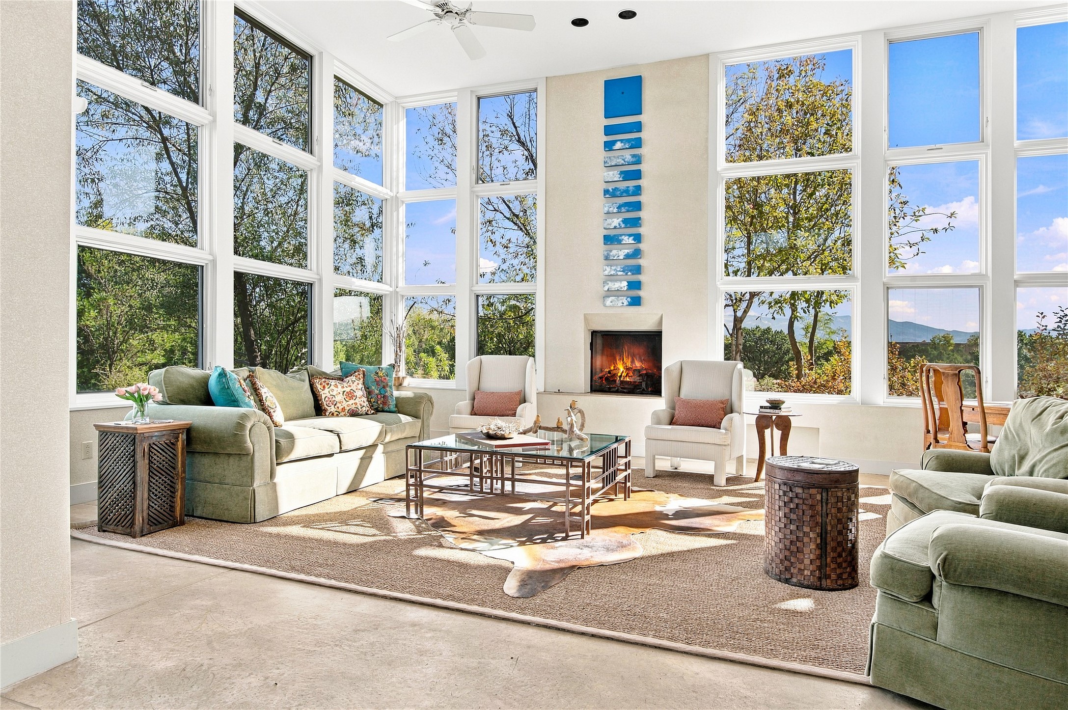 Living room with floor-to-ceiling windows, a lit fireplace, and views of trees and distant mountains.