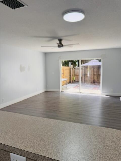 Empty living area with a ceiling fan and sliding glass doors opening to a fenced patio.