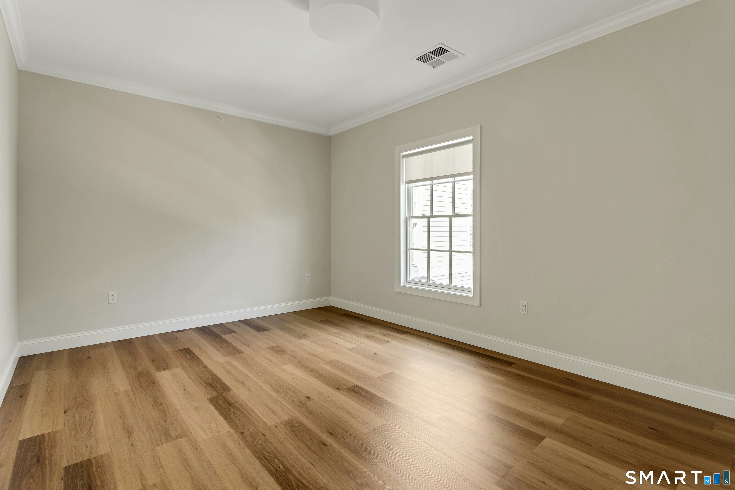 Empty room with wide-plank wood floors, neutral walls, and a single shaded window.