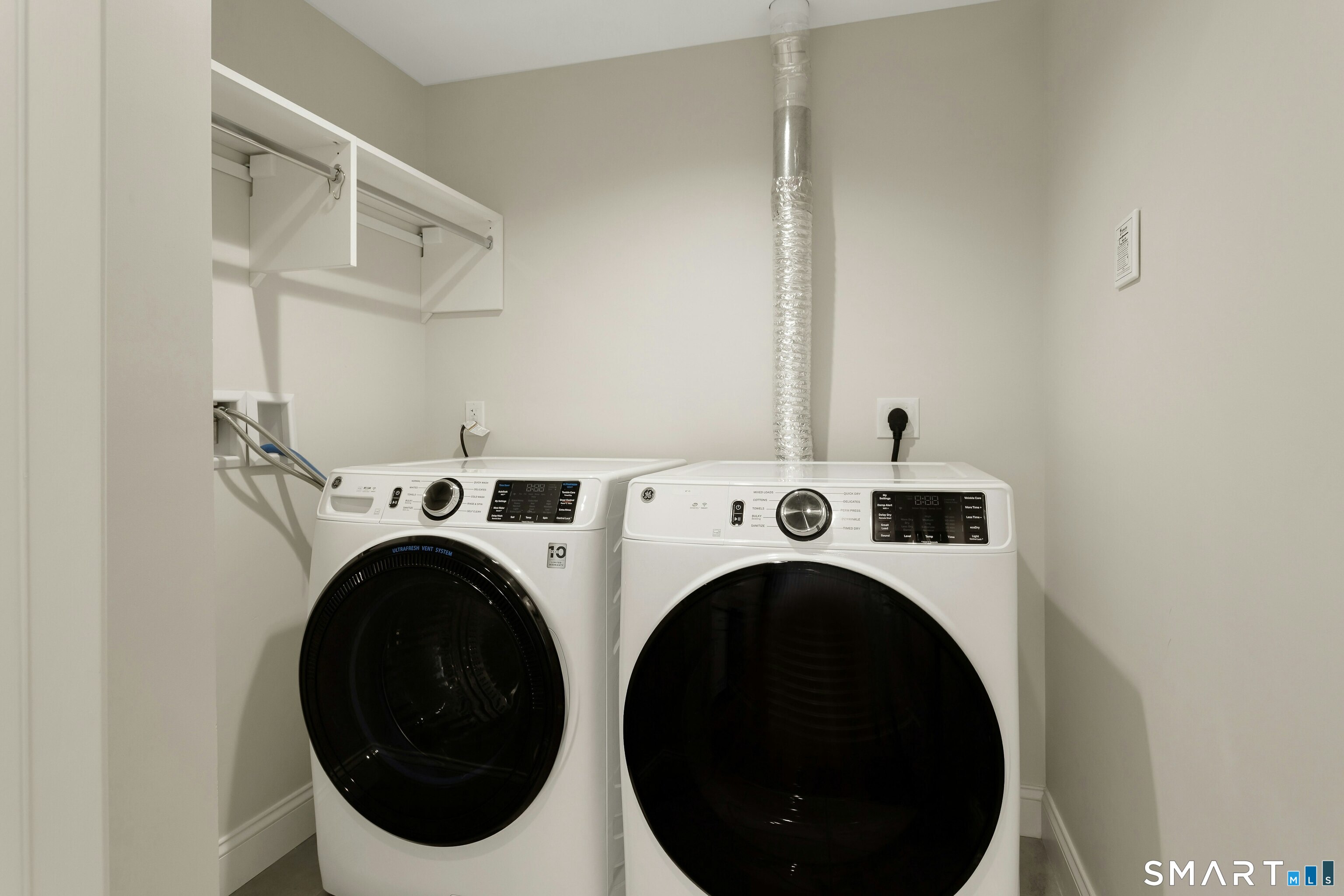 Laundry room with side-by-side front-loading washer and dryer beneath wall-mounted shelves.