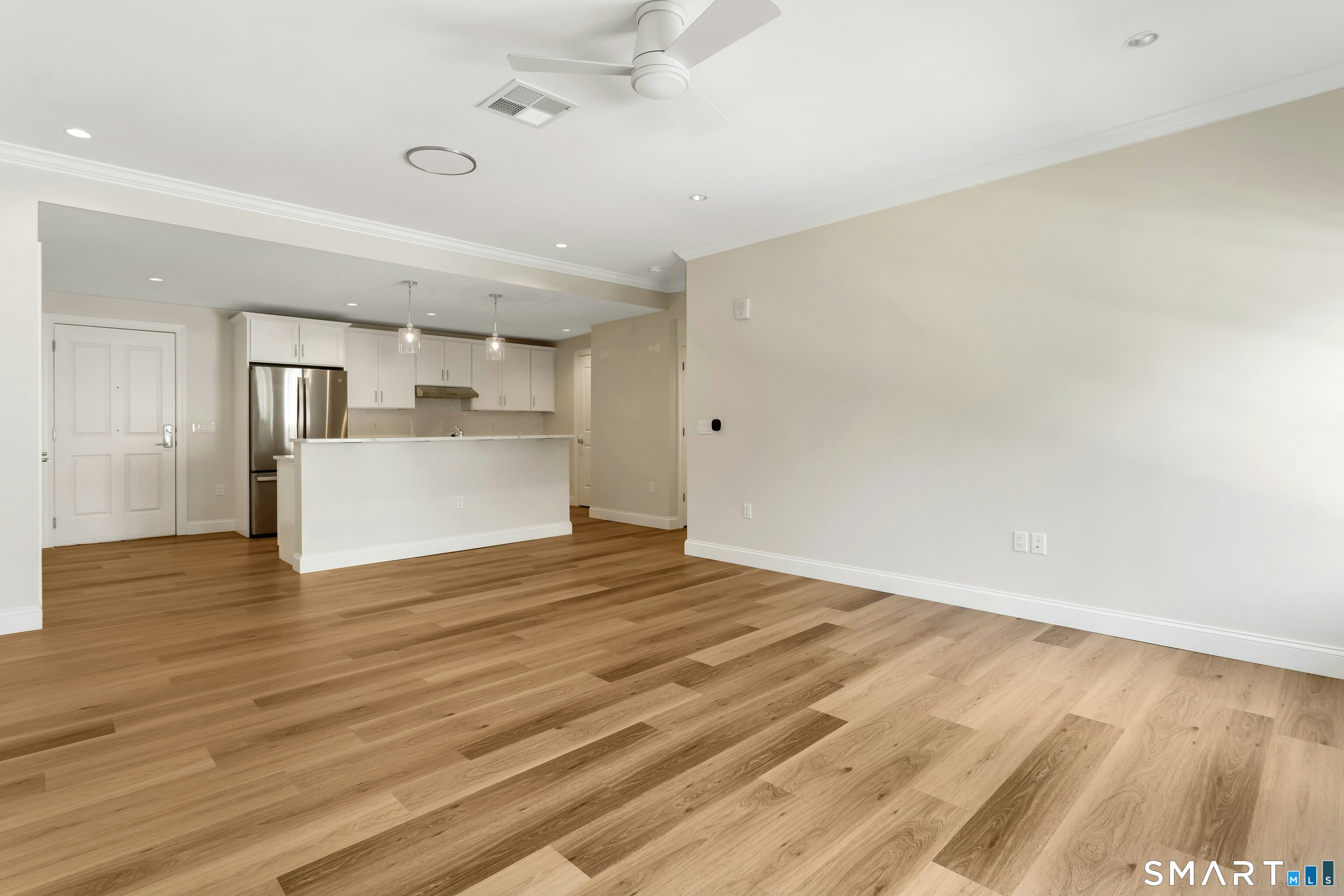 Unfurnished open-plan living area and kitchen with wide-plank wood floors and a white breakfast bar.