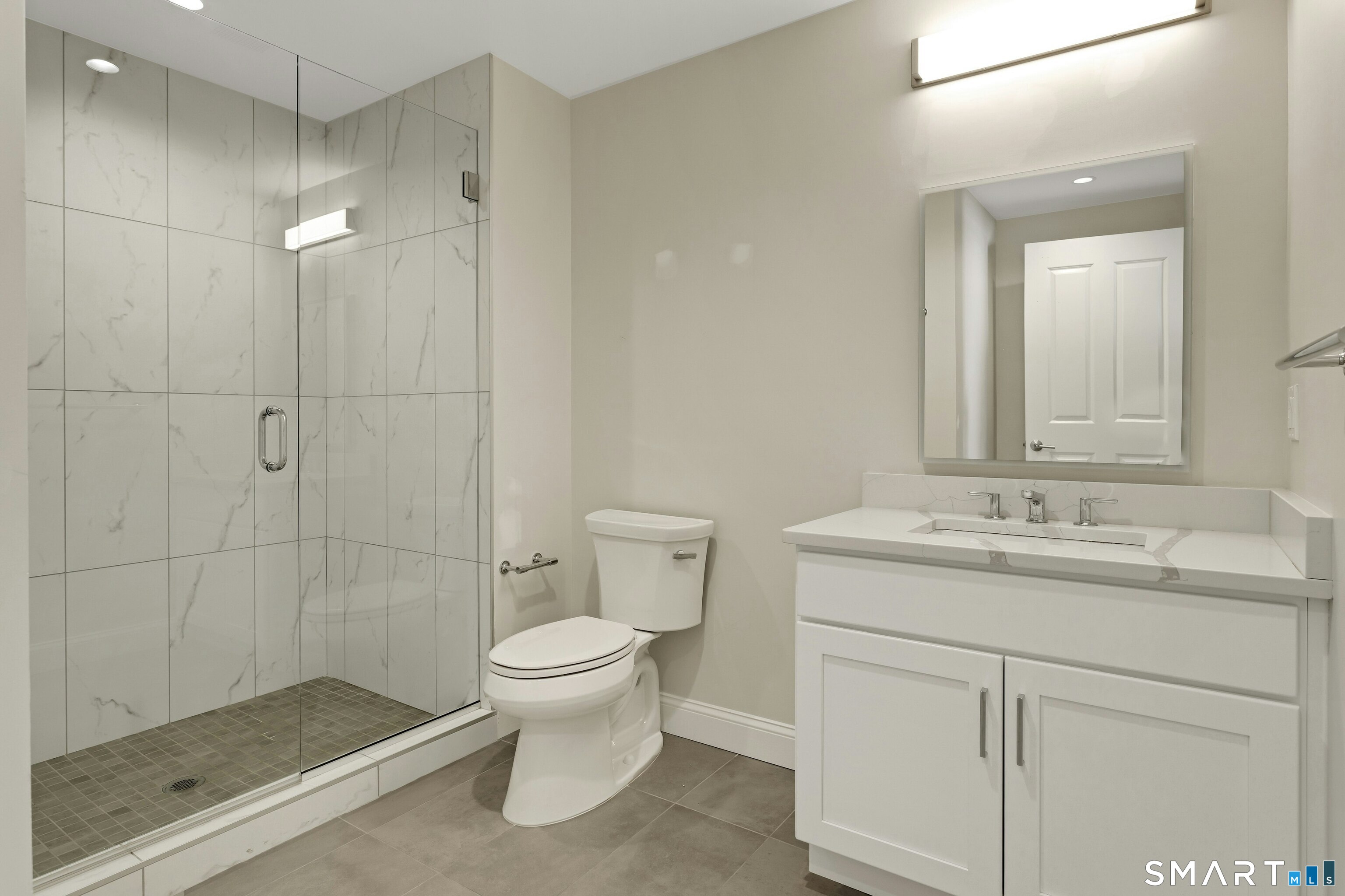 Modern bathroom with a glass-enclosed marble-look shower, white vanity, and gray tile floor.
