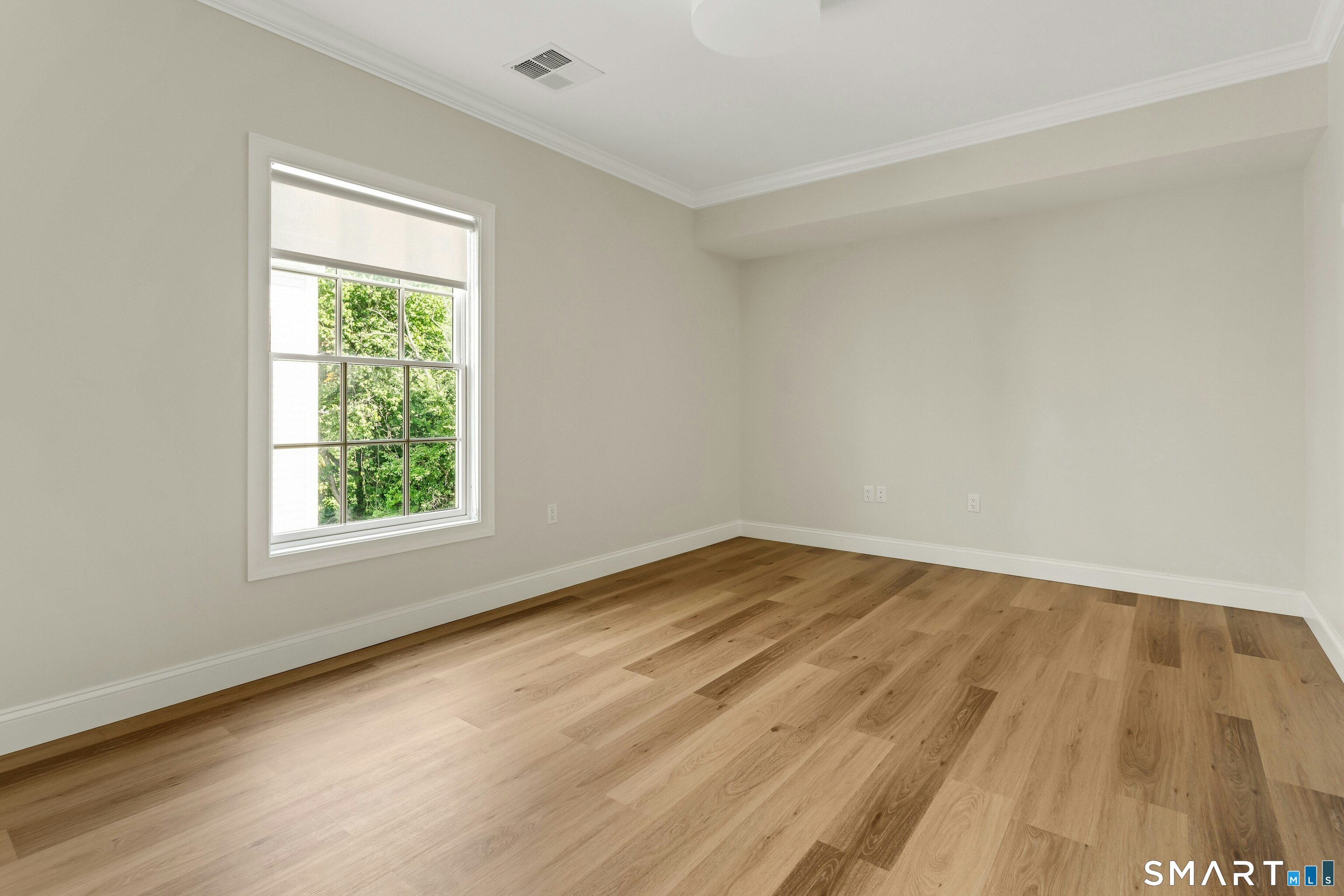 Empty room with light wood floors and a large window overlooking trees.