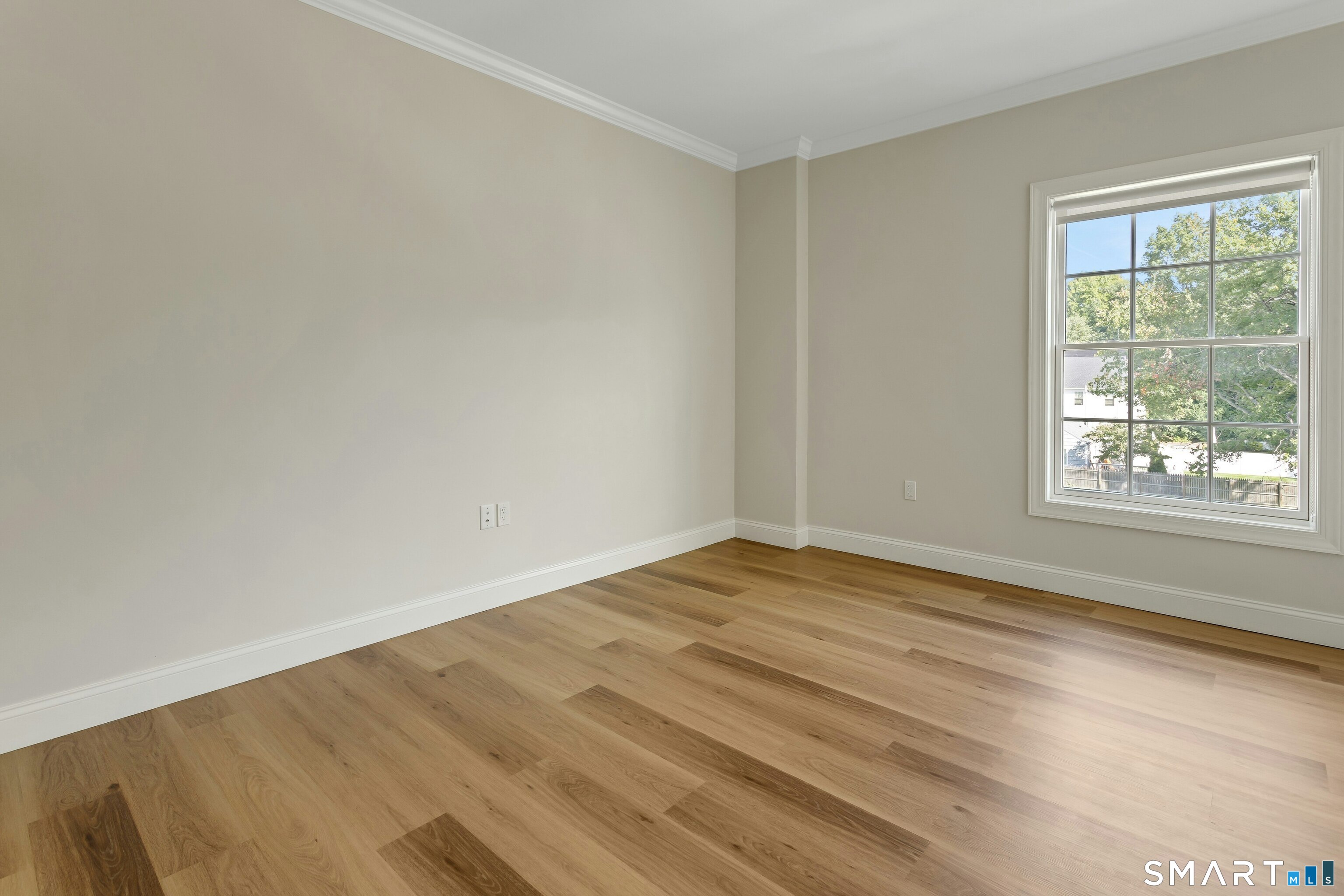 Vacant room with wide-plank wood floors and a large window overlooking leafy trees.