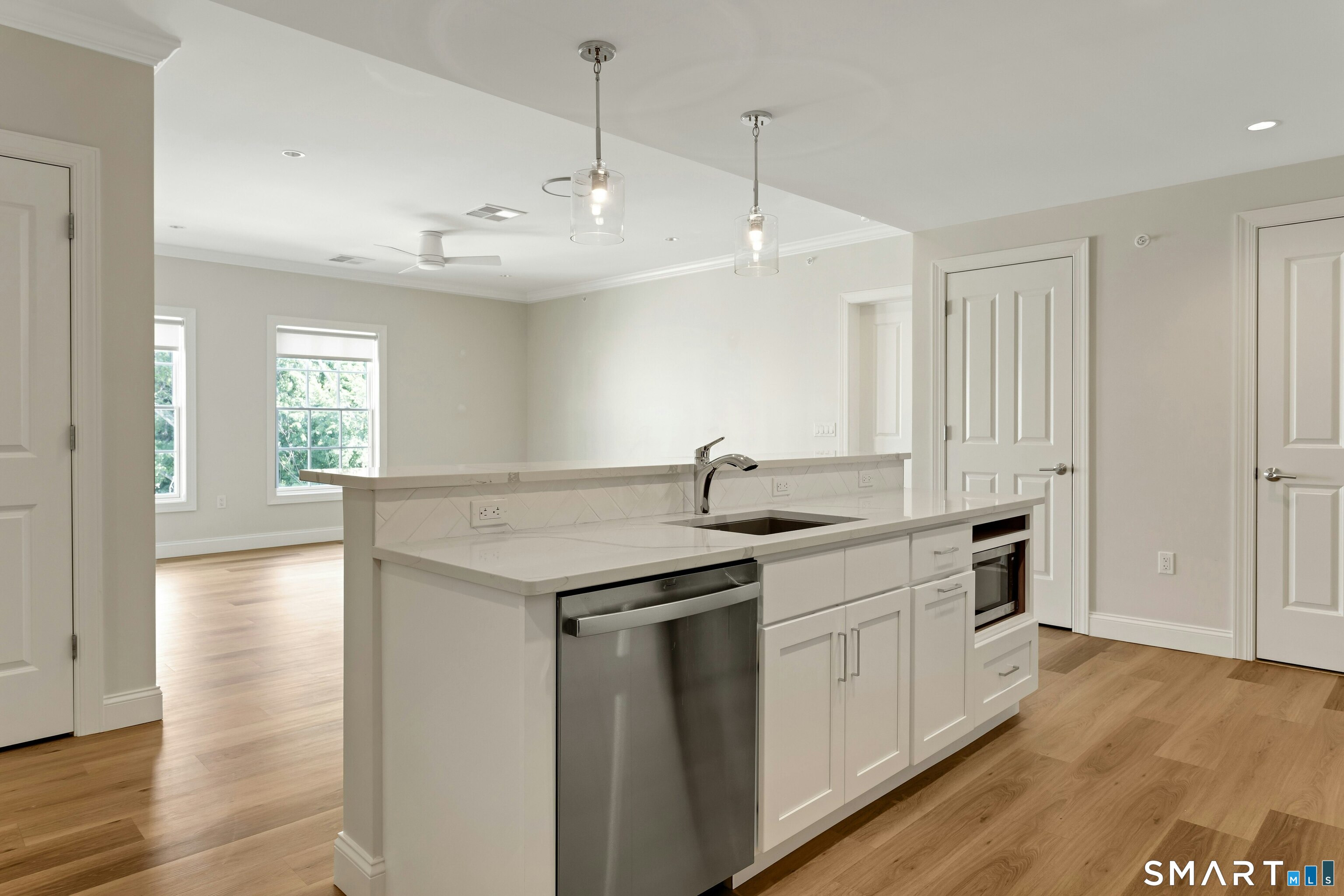Vacant kitchen with a large quartz island, white shaker cabinets, and stainless steel appliances.