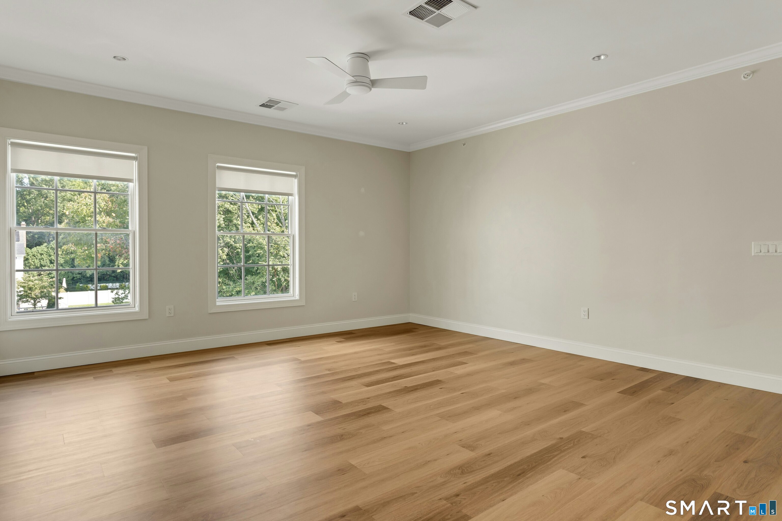 Empty room with wood floors, two shaded windows, and a ceiling fan.