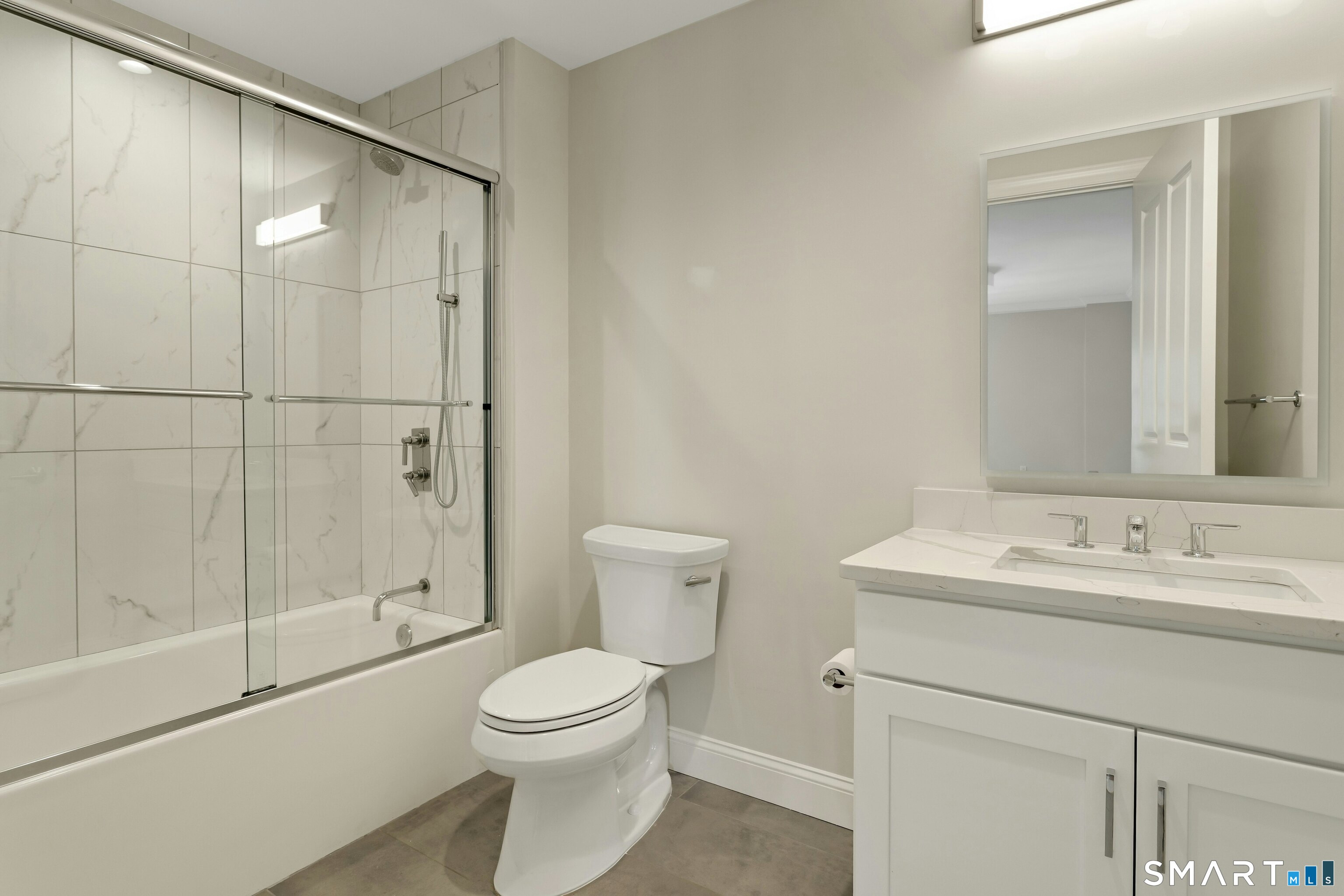 Bathroom with a glass-enclosed tub and shower, marble-look tile, and white vanity.