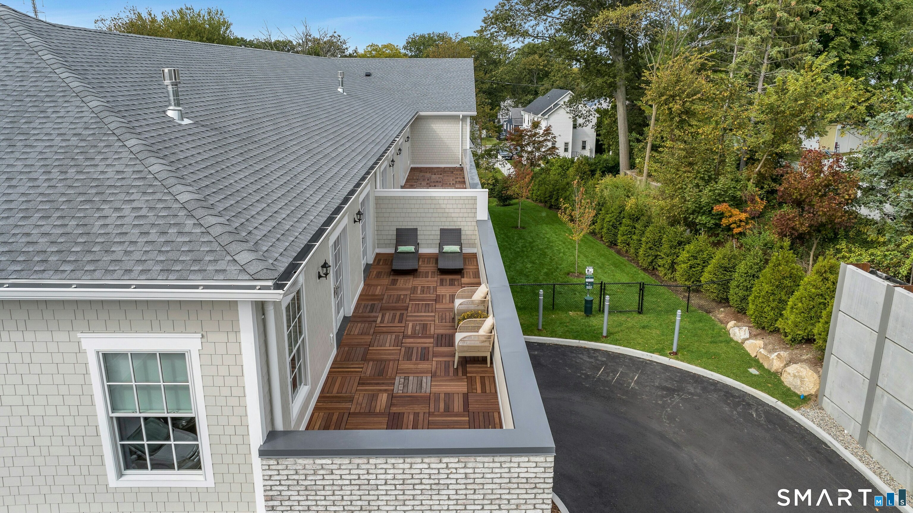 Condo rooftop terrace with wood tile flooring and lounge chairs overlooking a landscaped lawn.