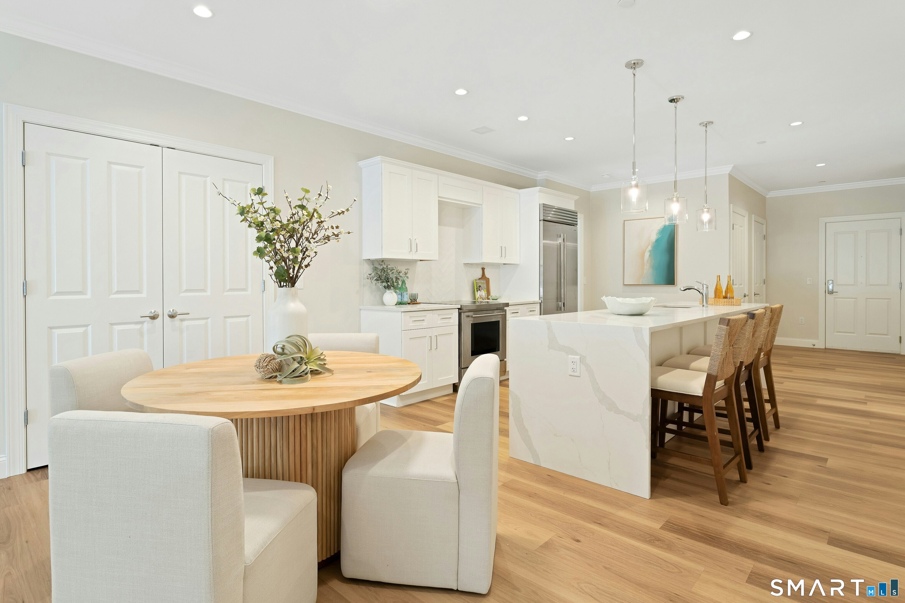 Open-plan kitchen and dining area with a marble island, white cabinetry, and round wood table.