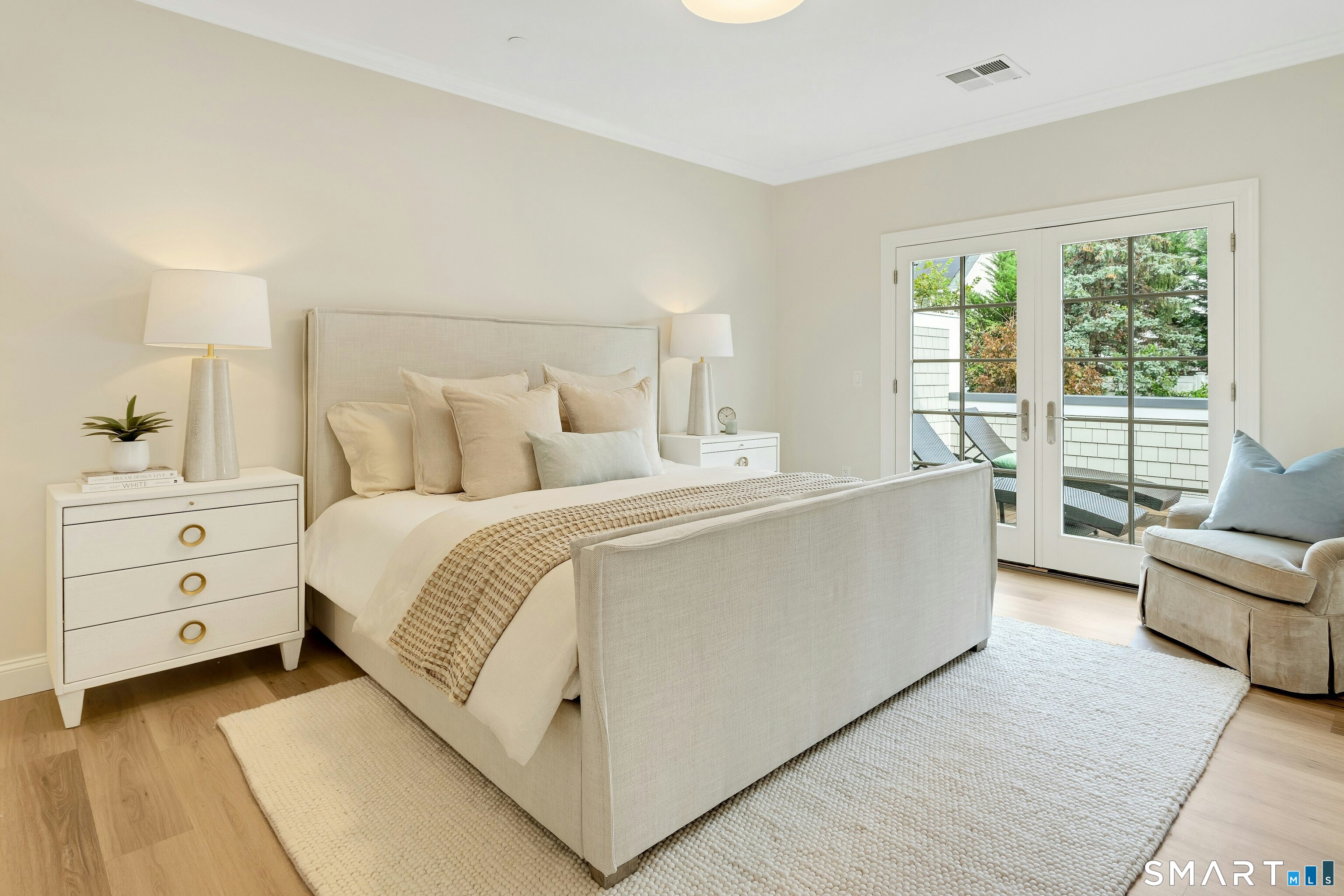 Neutral bedroom with an upholstered bed and French doors opening to a tree-lined balcony.