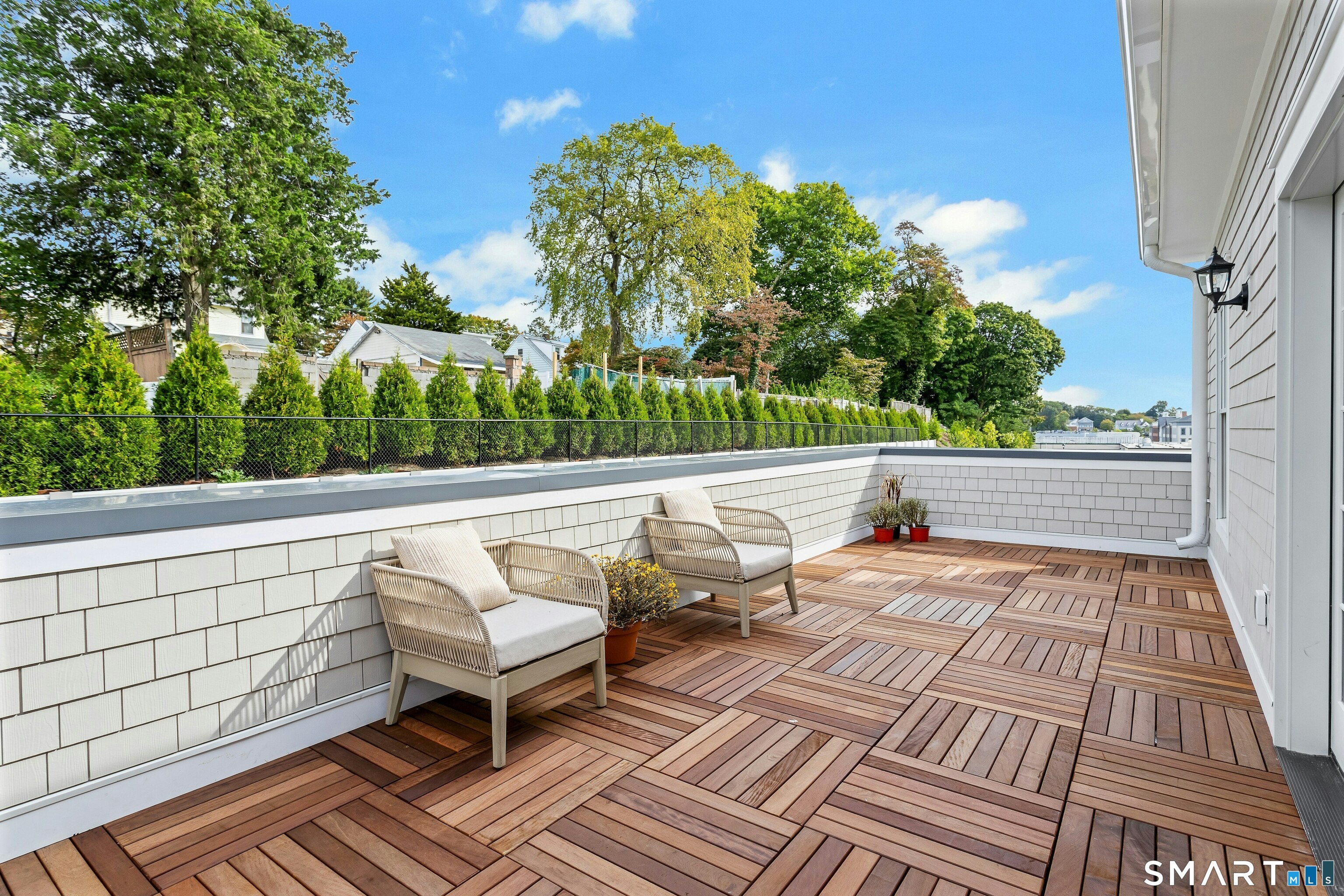 Elevated terrace with patterned wood decking, two cushioned chairs, and a leafy hedge.
