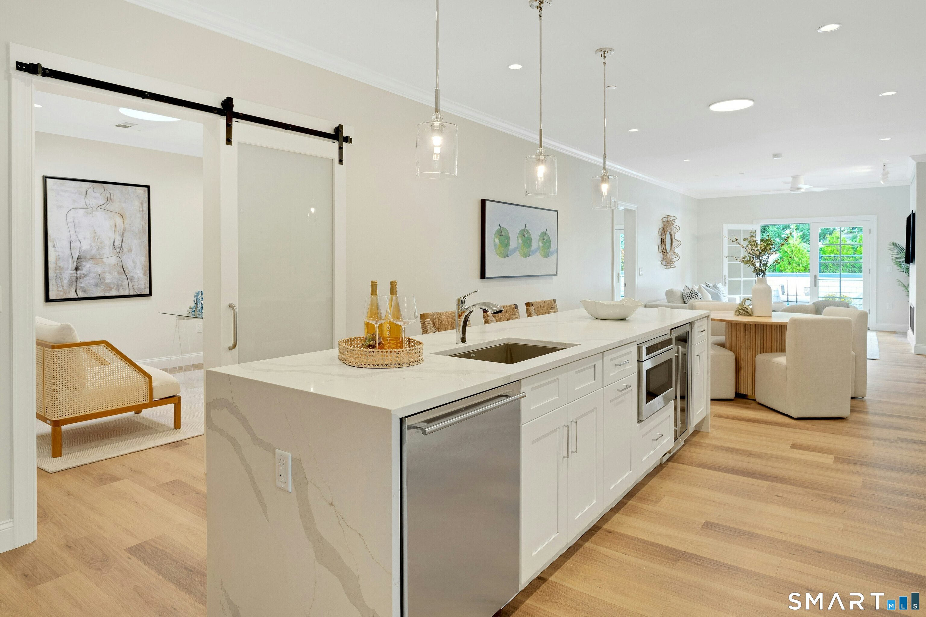 Open kitchen with a large marble island and stainless appliances, looking toward a bright living area and balcony.