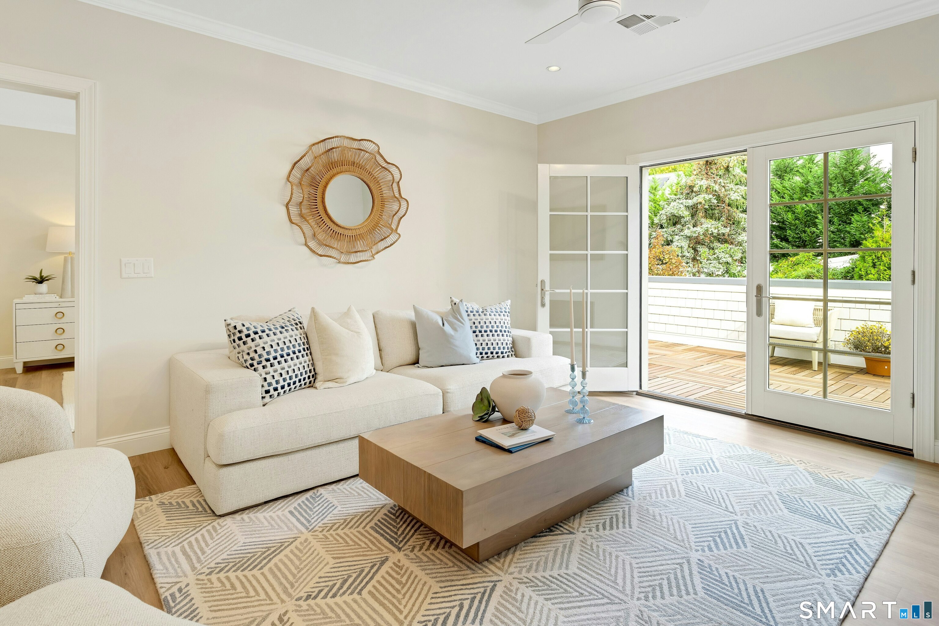 Bright living room with a cream sectional and open French doors to a wood-decked balcony.