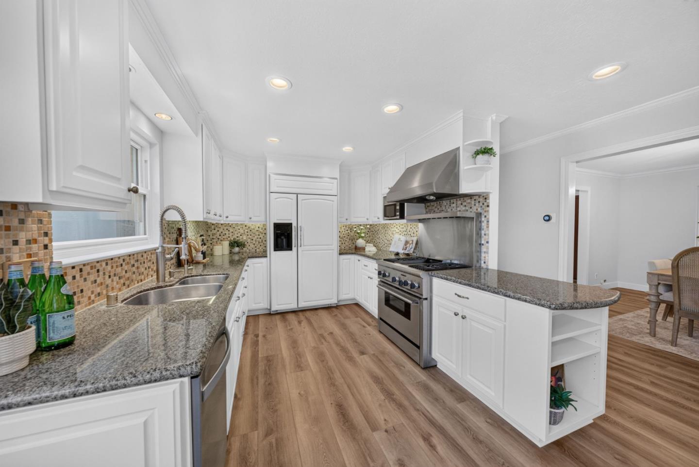 Bright kitchen with white cabinets, granite counters, mosaic tile backsplash, and stainless steel range.