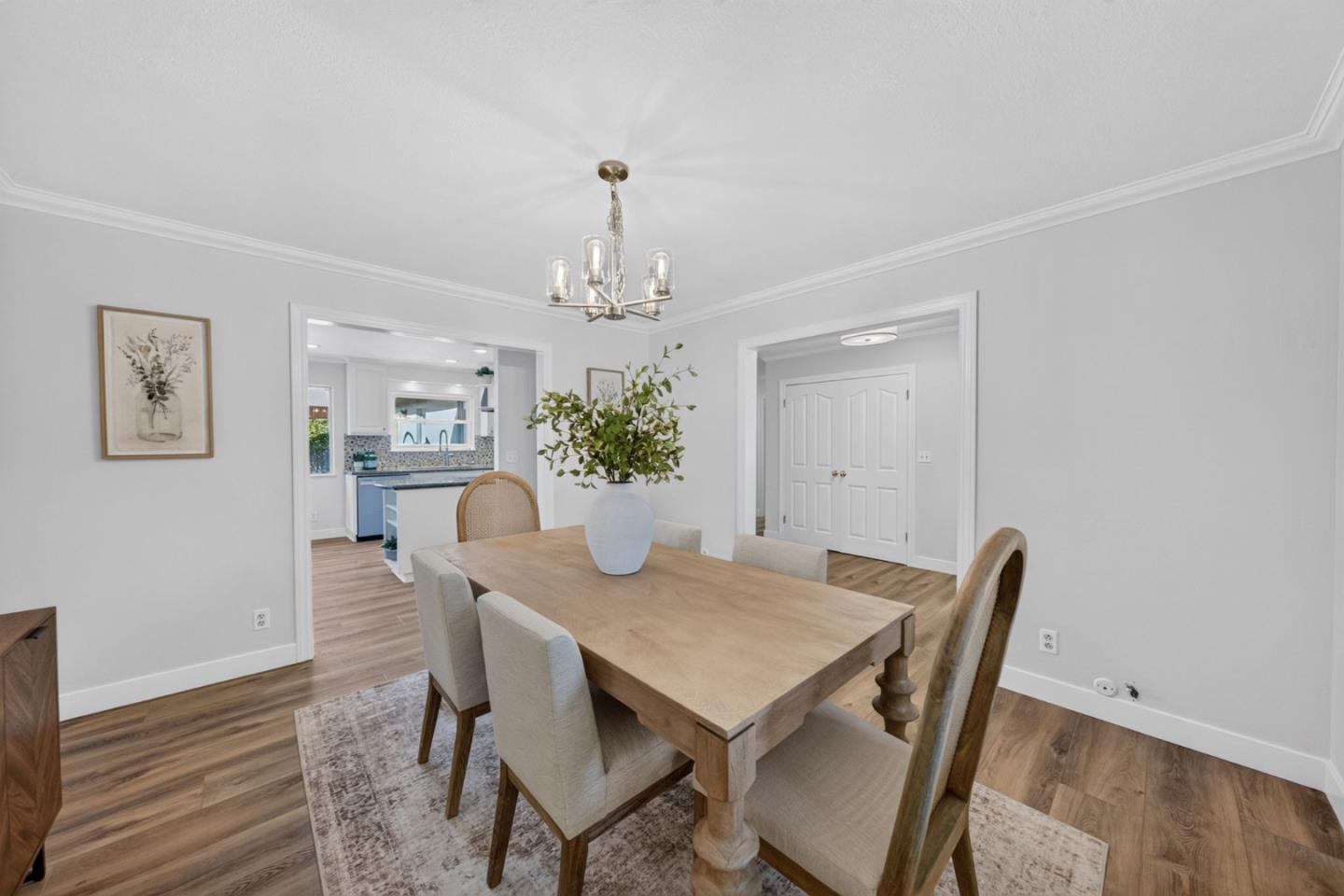 Staged dining room with a wood table, upholstered chairs, and an open view into the kitchen.