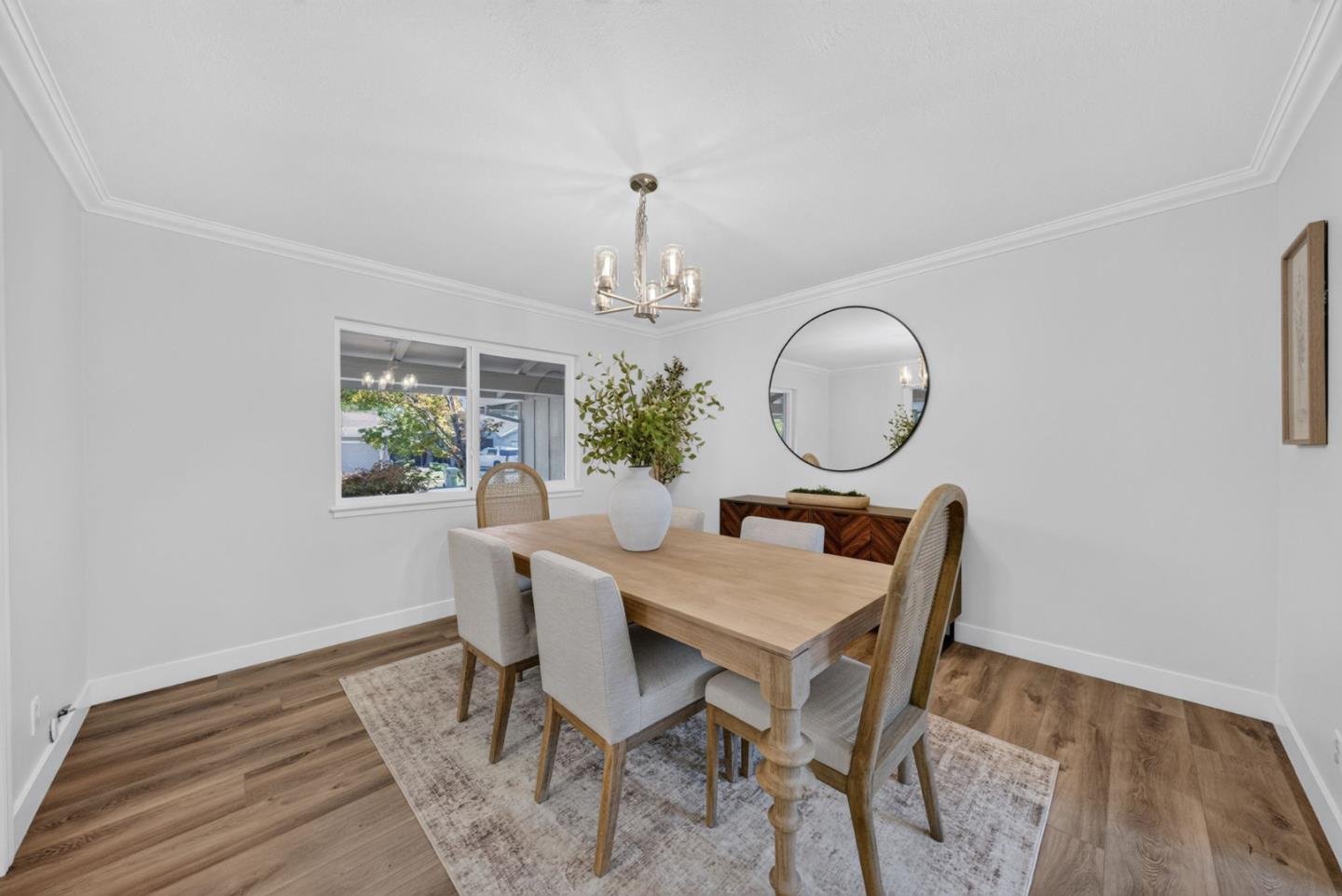 Dining room with a wooden table, upholstered chairs, round mirror, and leafy centerpiece.