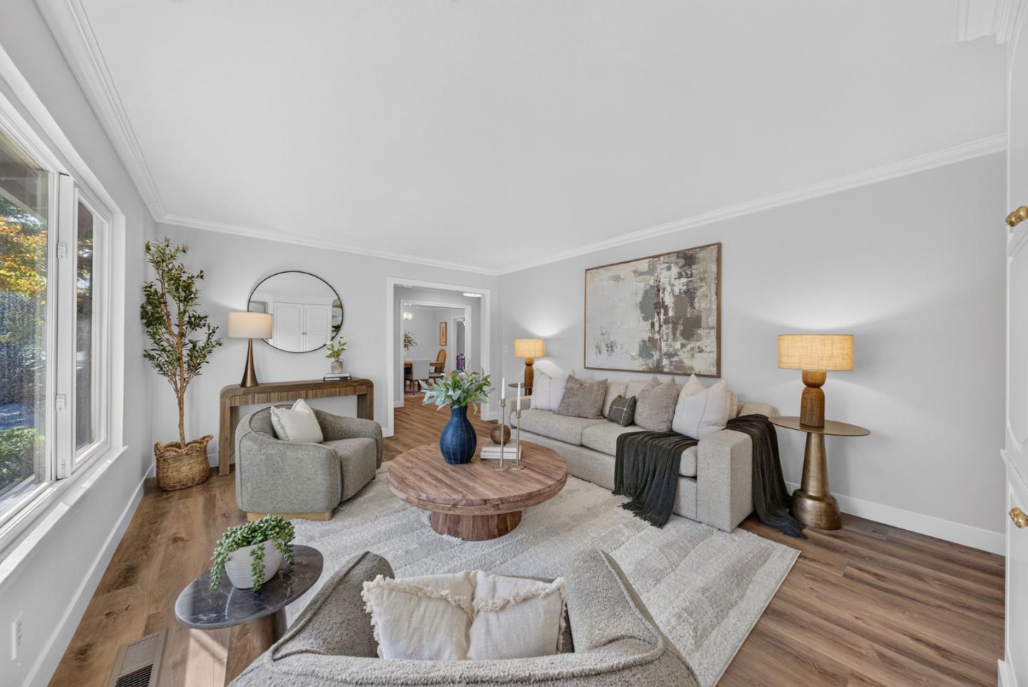 Staged living room with a gray sofa and armchair, round wood coffee table, and large window.