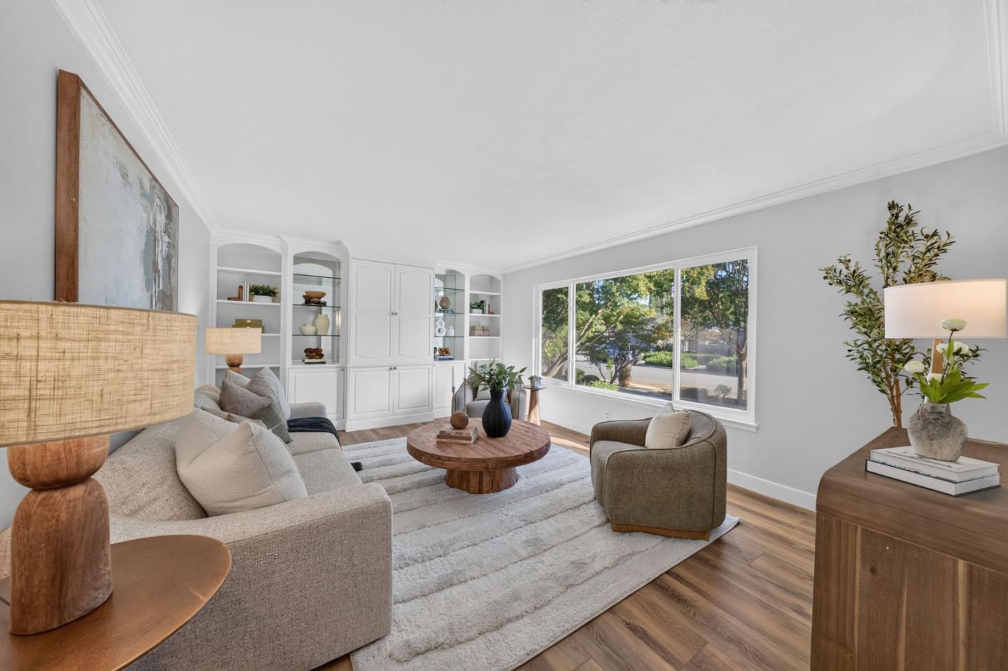 Staged living room with built-in white shelves and large windows overlooking leafy trees.
