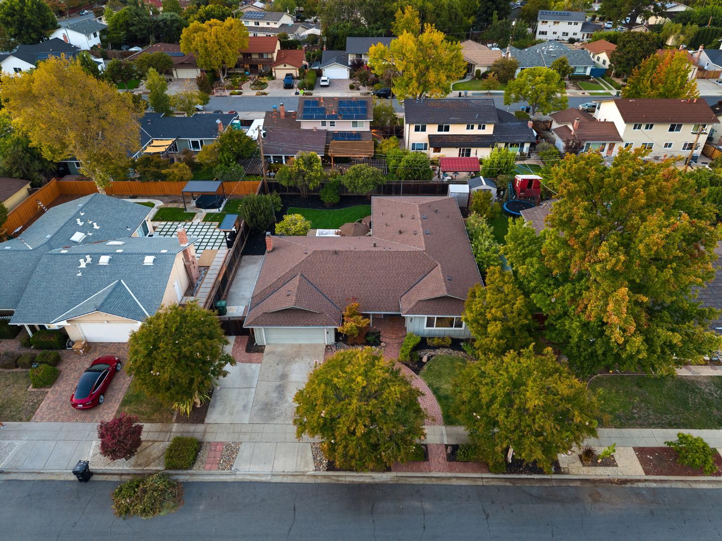 Aerial view of a single-story home with a brown roof and landscaped yard among autumn trees.