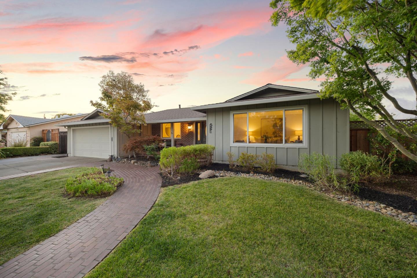 Single-story home with an attached garage, curved brick walkway, and illuminated front window at dusk.