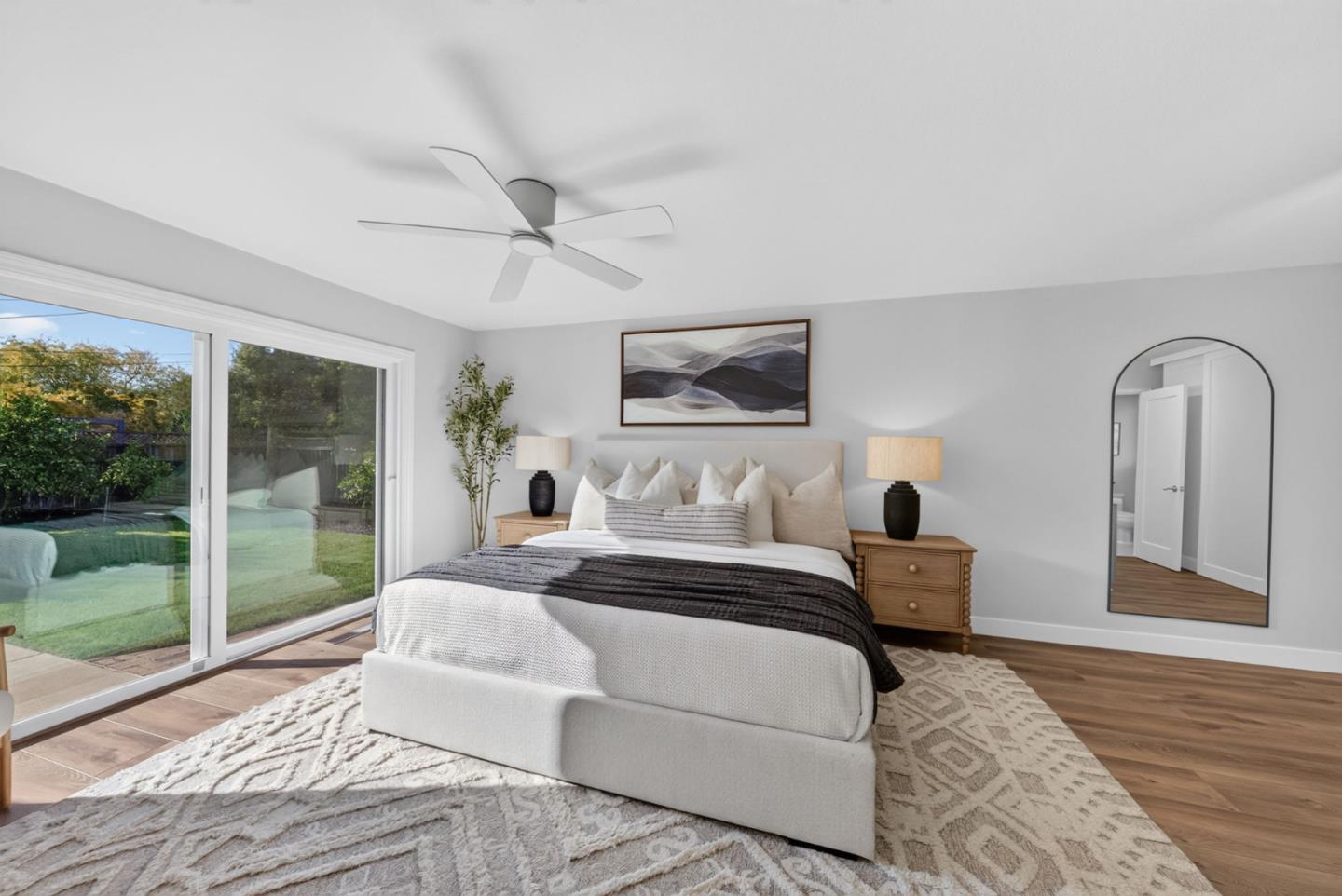 Staged bedroom with a white bed, ceiling fan, and sliding glass doors overlooking the backyard.