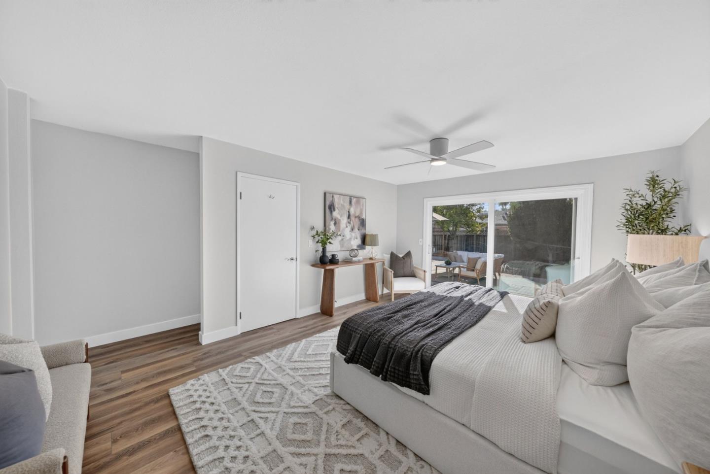 Staged bedroom with a large white bed, patterned rug, and sliding glass doors to a patio.