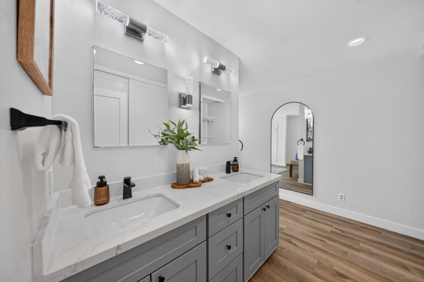 Bathroom with a gray double vanity, white veined countertop, and arched mirror.