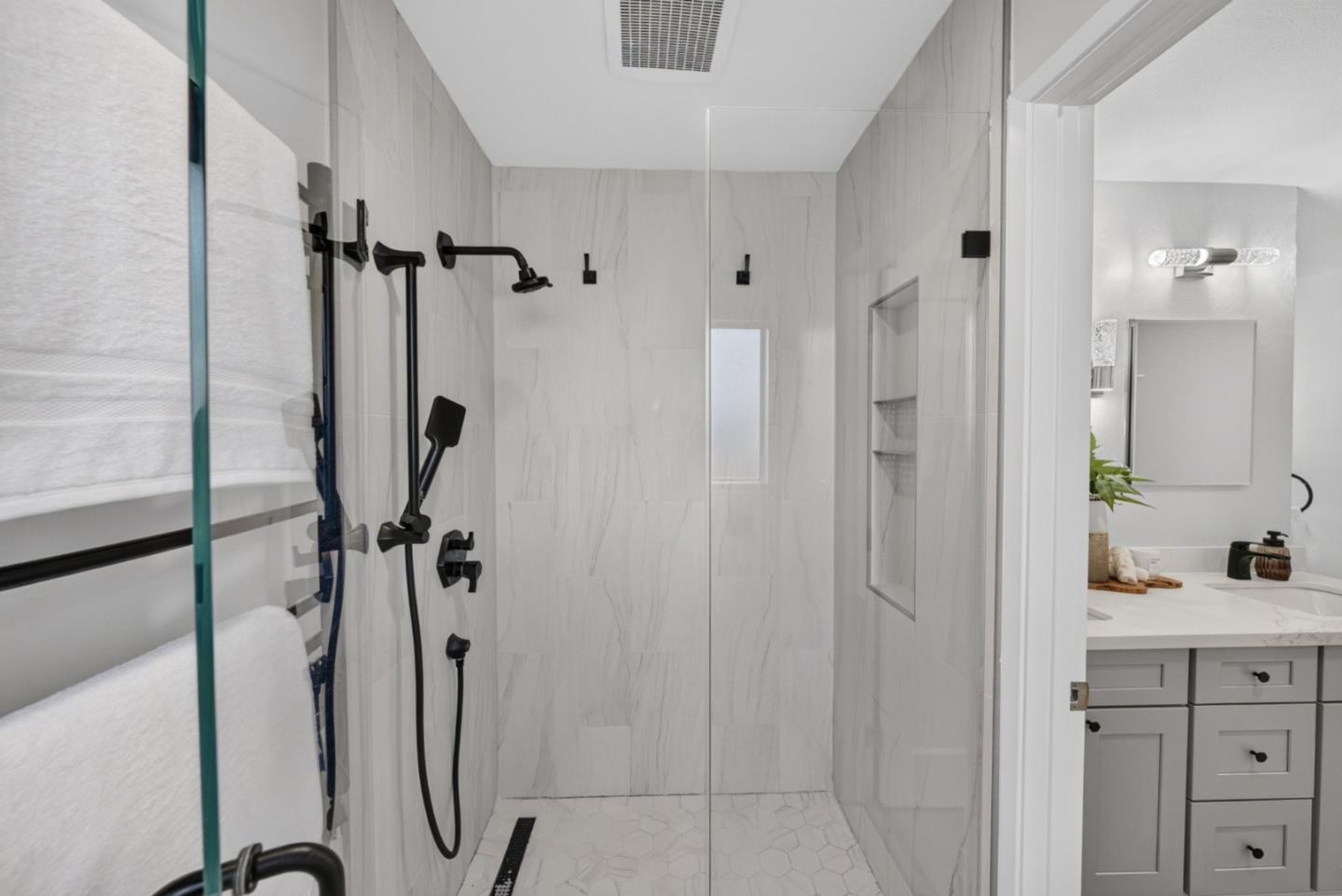 Bathroom with a glass-enclosed marble-look shower, black fixtures, and a gray vanity.