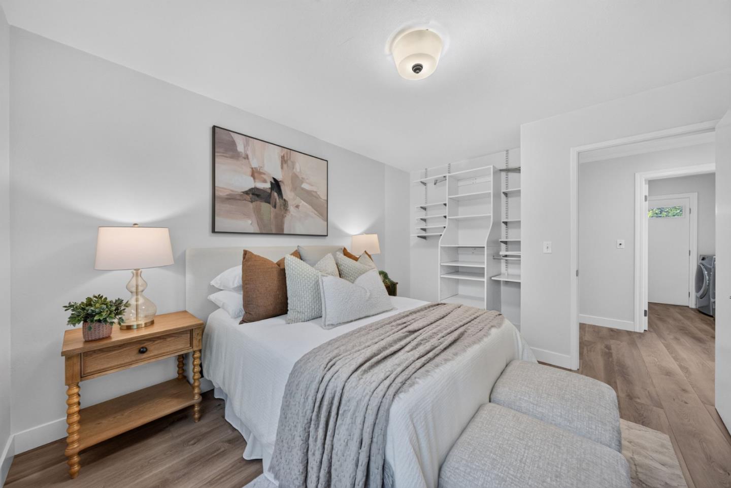 Staged bedroom with a white bed, built-in shelving, and wood floors.