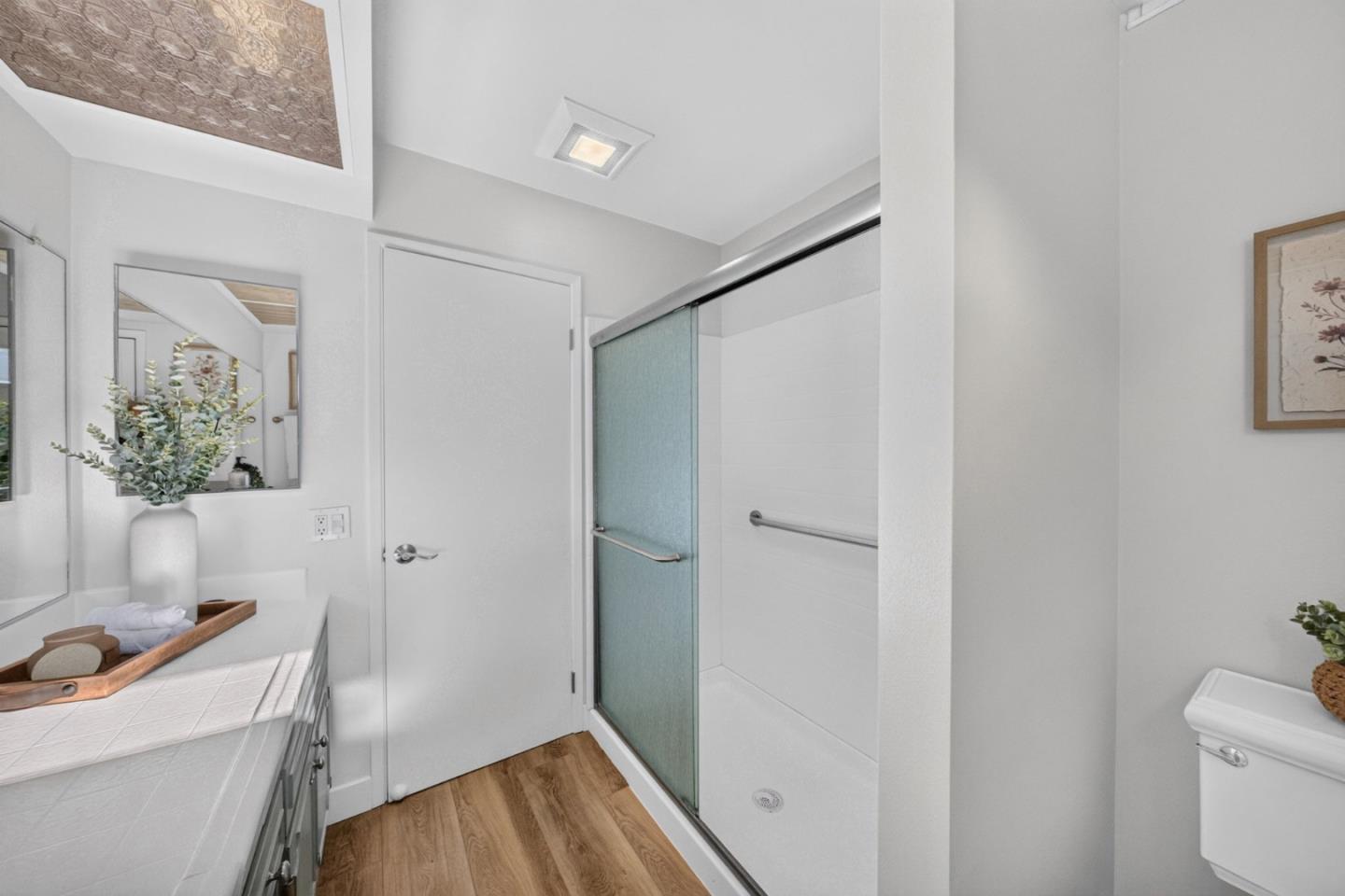 Bathroom with a glass shower, tiled vanity, and warm wood-look flooring.