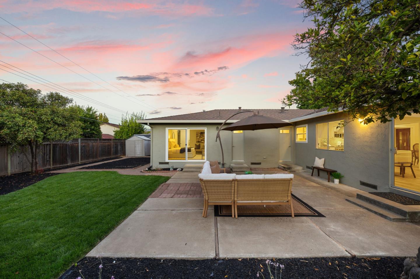 Home’s backyard patio at dusk with outdoor seating, a green lawn, and pink sunset sky.