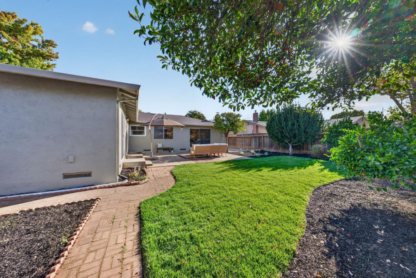 Backyard lawn and brick path leading to a shaded patio with outdoor seating.