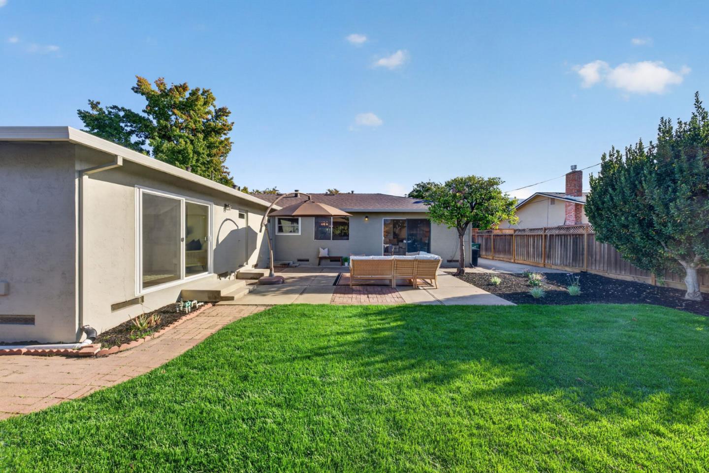 Home’s backyard with a broad lawn and paved patio furnished with outdoor seating and an umbrella.