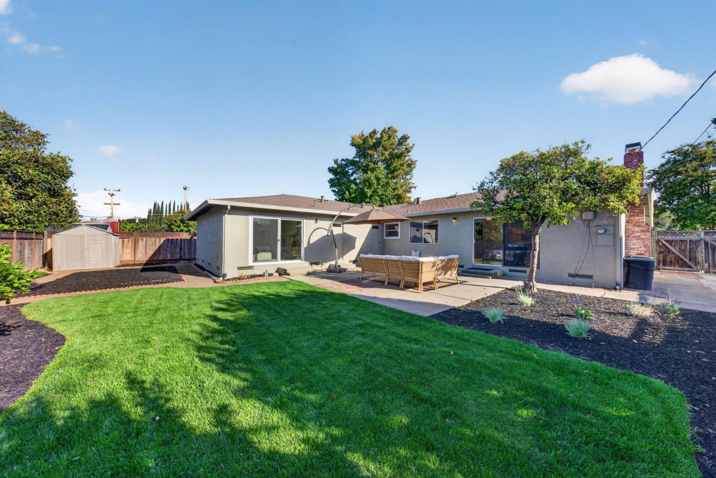 Single-story home's backyard with a green lawn and patio dining area.