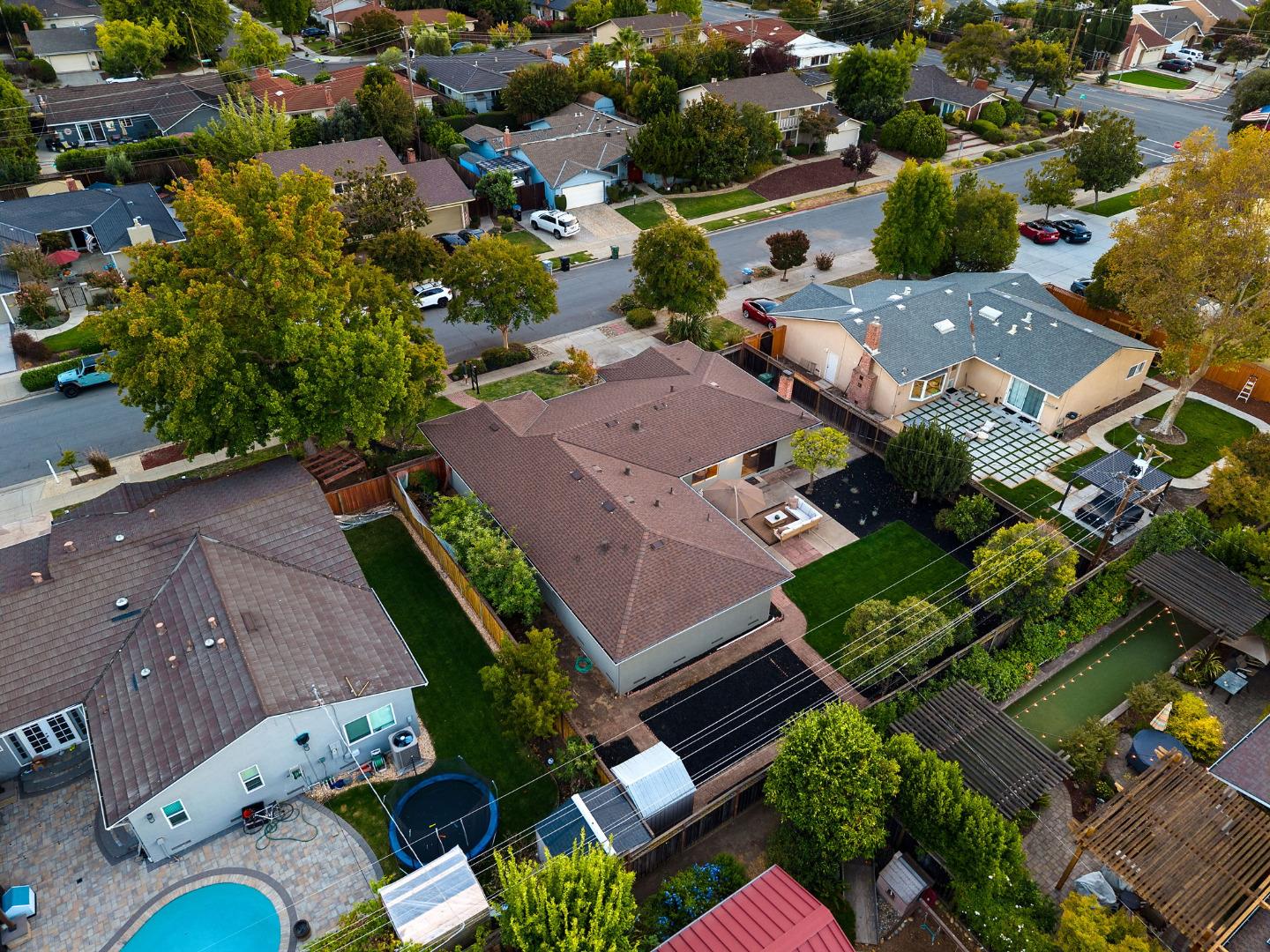 Aerial view of a gray single-story home with a brown roof among neighborhood homes and yards.