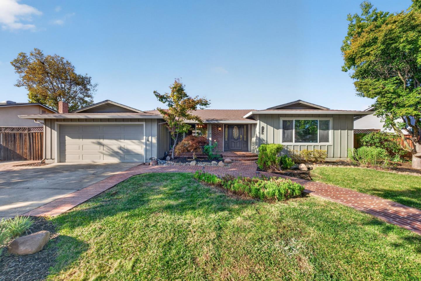 Single-story home with a two-car garage and curved brick walkway through the front garden.