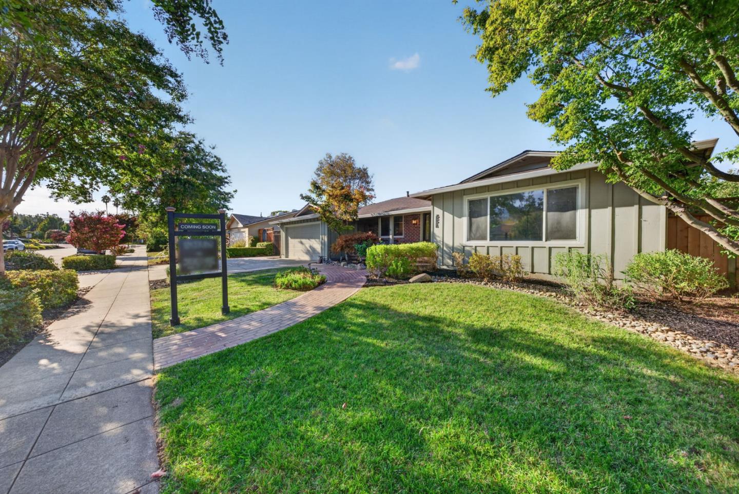 Single-story home with a broad lawn, mature trees, and a brick walkway to the entrance.