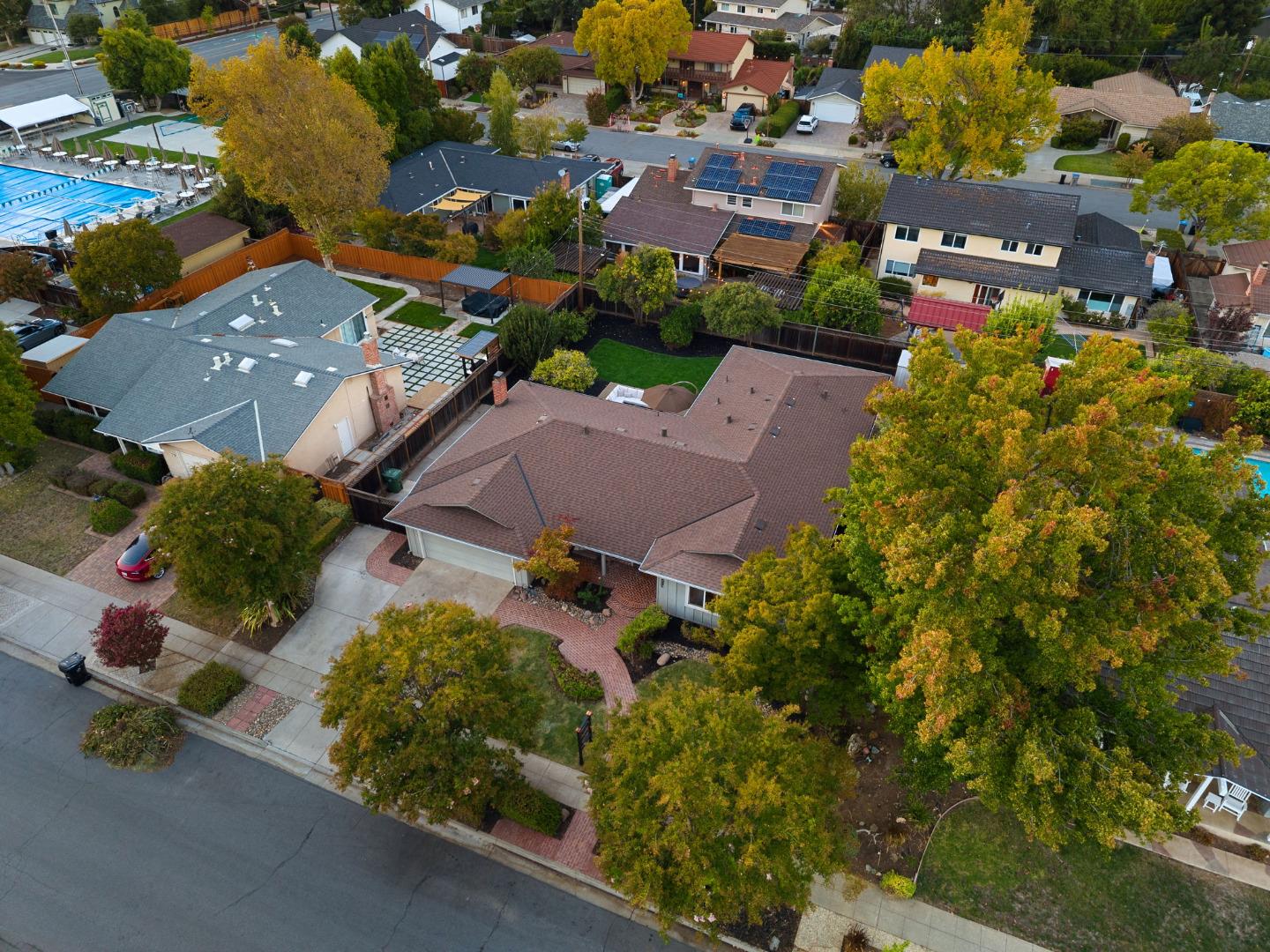 Aerial view of a single-story home with a reddish-brown roof, brick walkway, and mature autumn trees.
