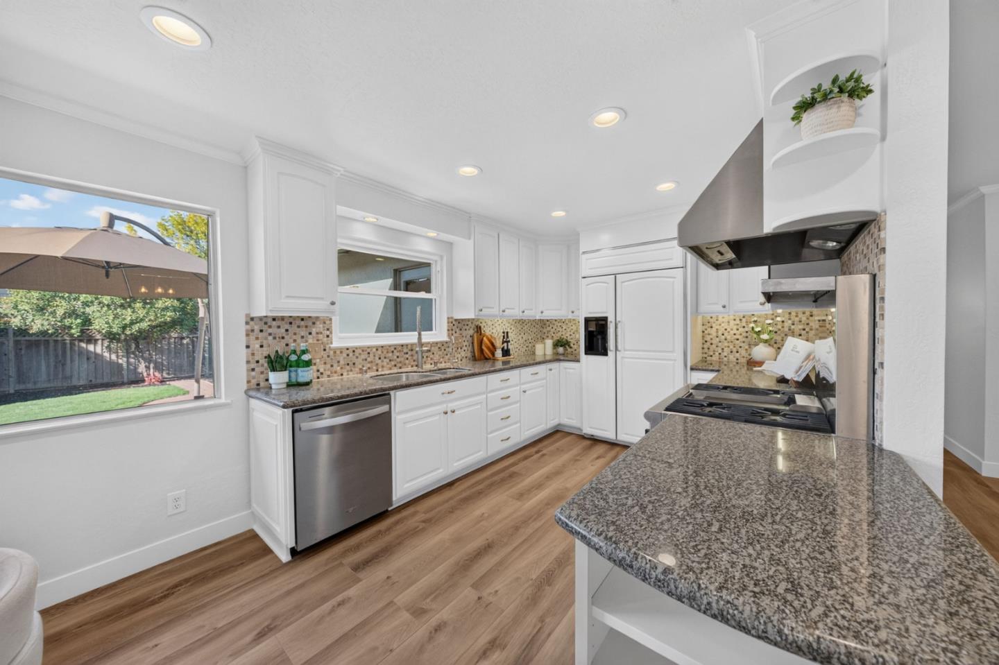 Bright kitchen with white cabinets, granite counters, mosaic backsplash, and a window overlooking the backyard.