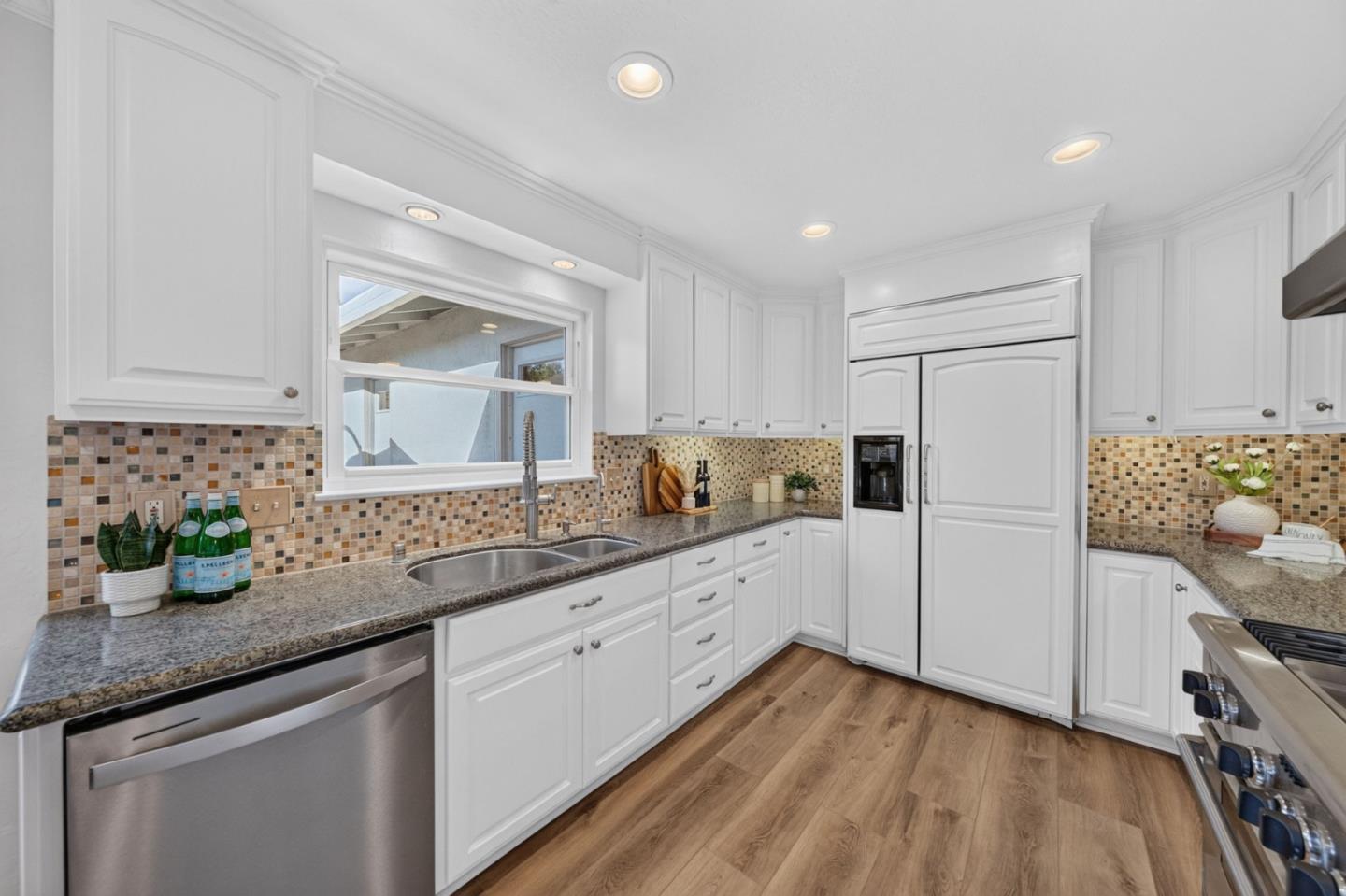 Bright white kitchen with granite counters, mosaic backsplash, and a window above the double sink.