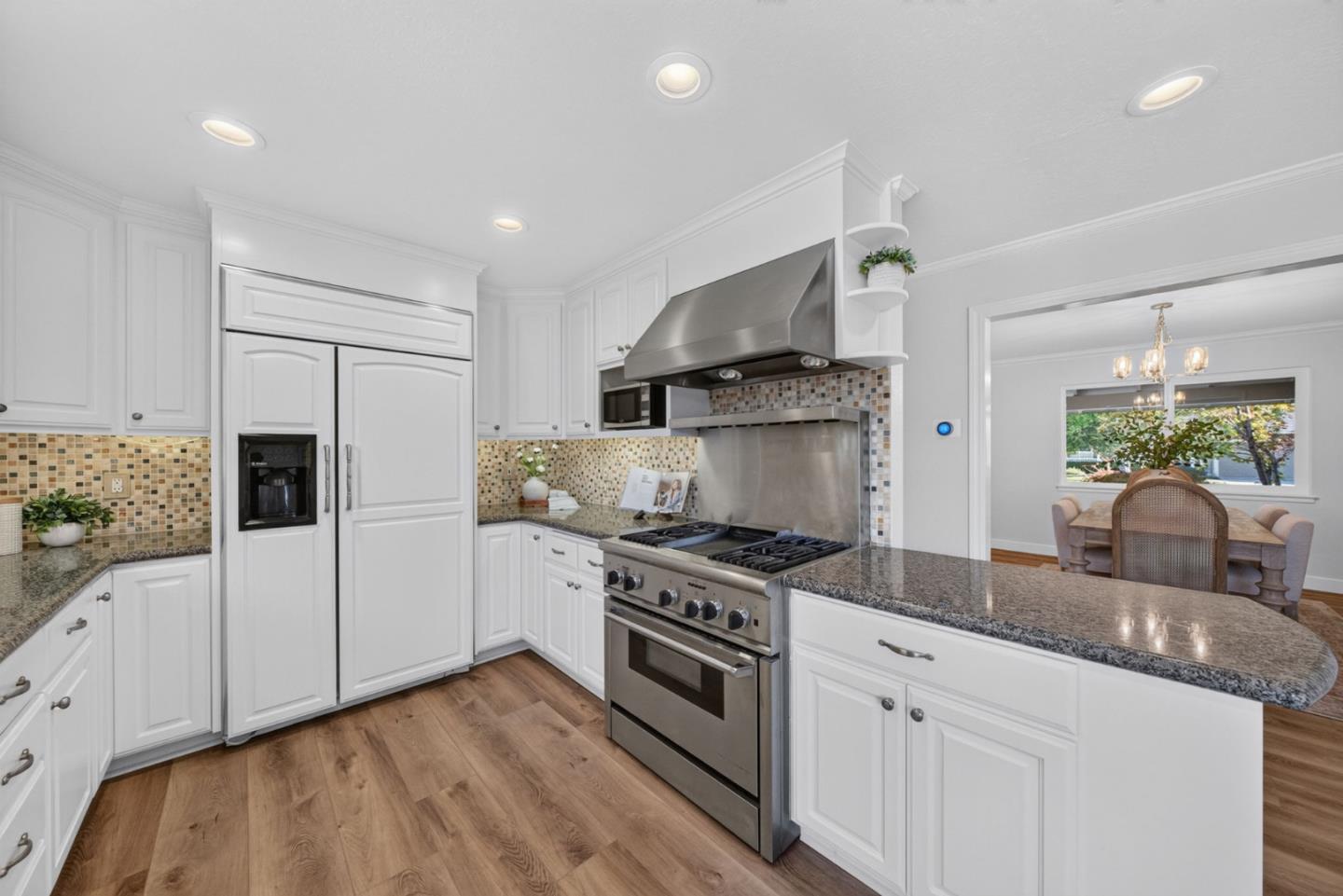 Kitchen with white cabinets, granite counters, stainless steel appliances, and a mosaic tile backsplash.