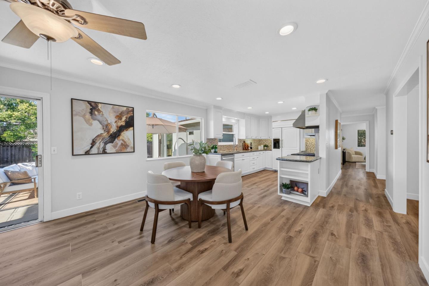 Open kitchen and dining area with white cabinets, a central island, and a round table by sliding glass doors.