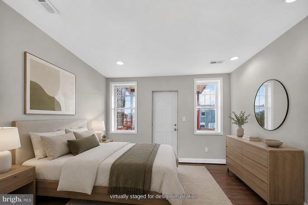 Virtually staged bedroom with a large neutral bed, wood dresser, oval mirror, and two tall windows.