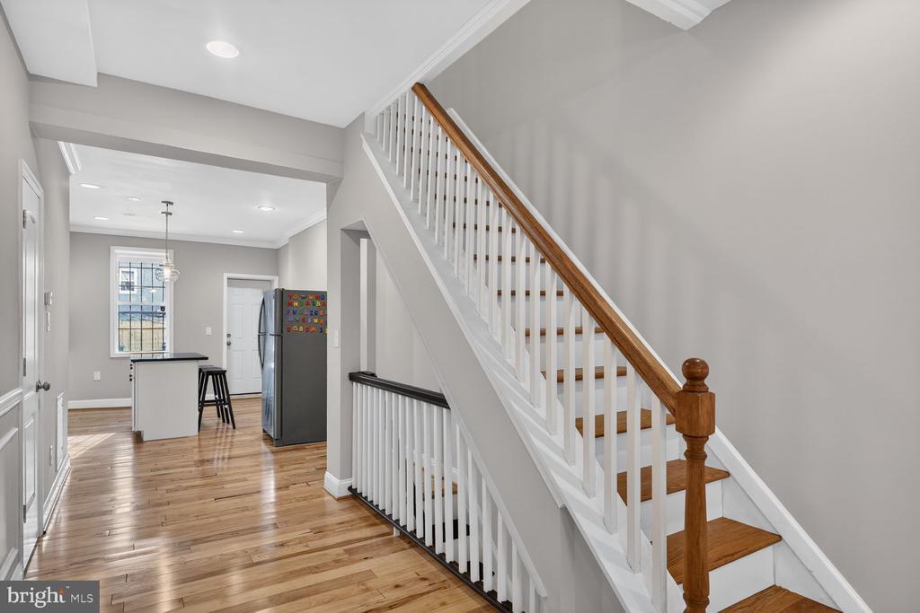 Entry hall with hardwood floors and a white staircase with a wood handrail, opening to the kitchen.