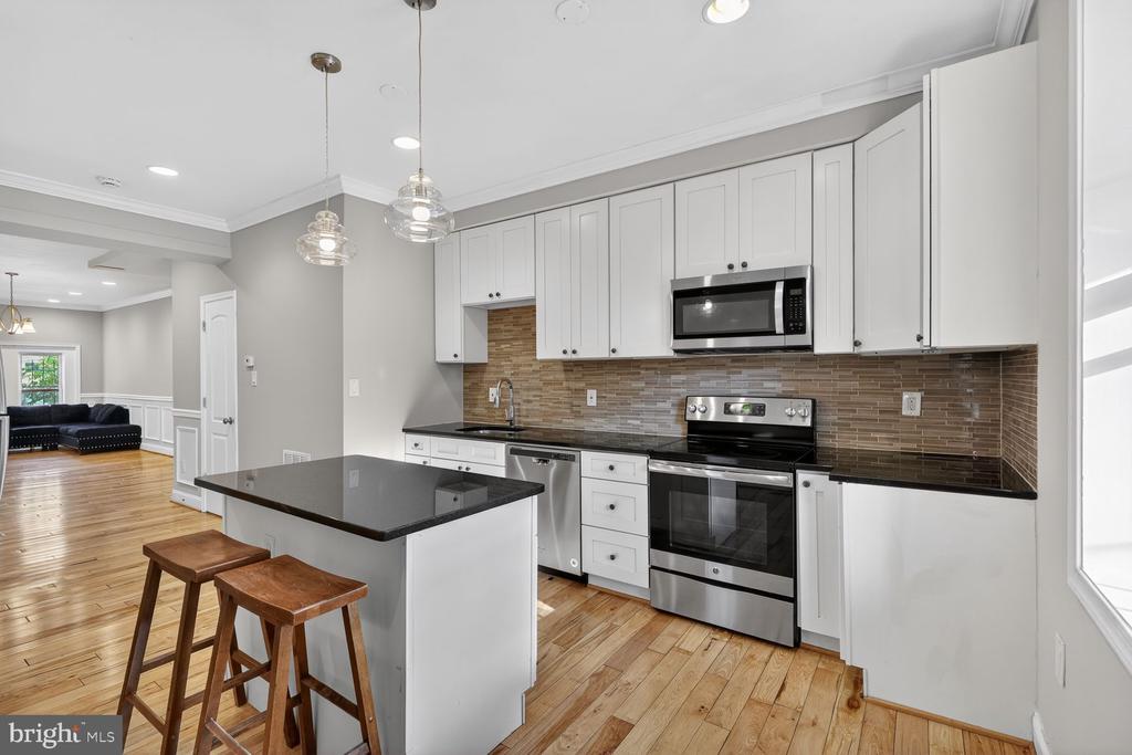 Kitchen with white cabinets, stainless steel appliances, a dark island, and hardwood floors.