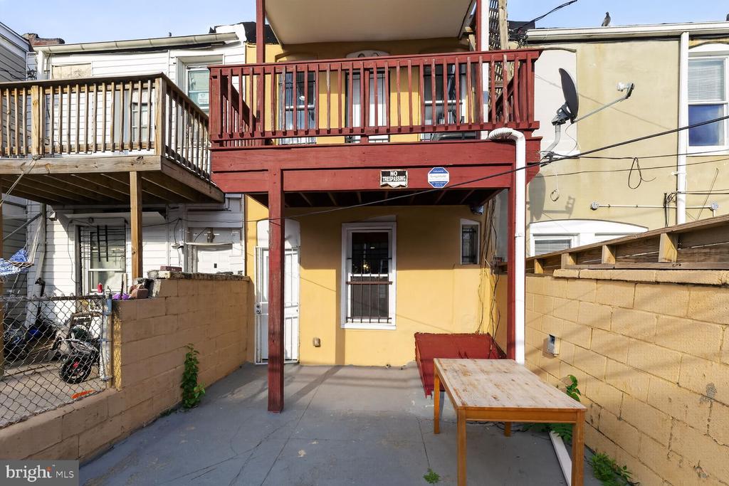 Rear patio with a red wooden balcony structure, tan walls, bench, and outdoor table.