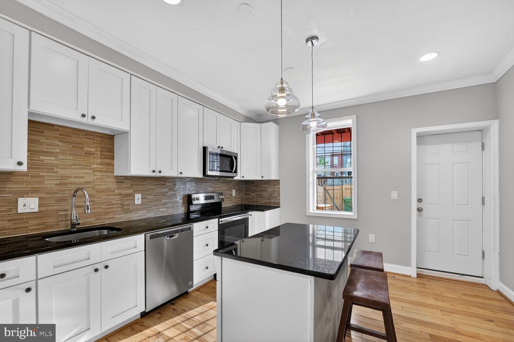 Kitchen with white cabinets, black countertops, stainless steel appliances, and an island with two stools.